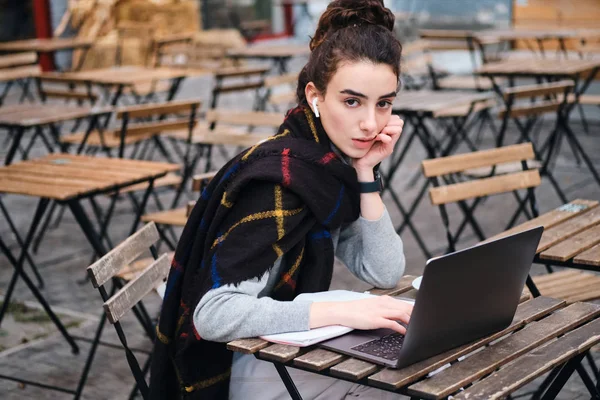 Mooie casual student meisje met sjaal studeren op laptop zelfverzekerd op zoek in camera in cafe op straat — Stockfoto