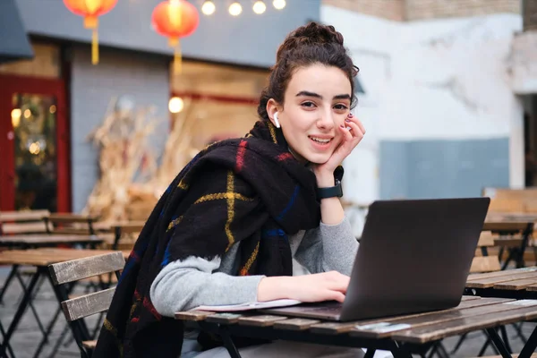 Vrij lachende student meisje met sjaal studeren op laptop gelukkig op zoek in camera in cafe op straat — Stockfoto