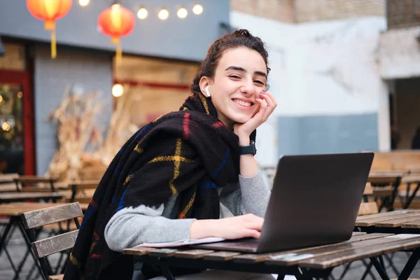 Vrij vrolijk student meisje met sjaal gelukkig studeren op laptop in cafe op straat — Stockfoto