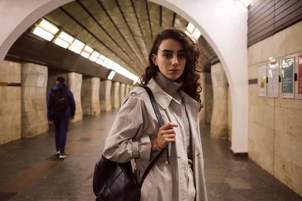 Piękny casual dziewczyna w płaszczu Trench z plecakiem starannie patrząc w aparacie na stacji metra — Zdjęcie stockowe