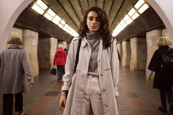 Menina elegante Pensive em casaco de trincheira com mochila sonhadoramente olhando na câmera na estação de metrô — Fotografia de Stock