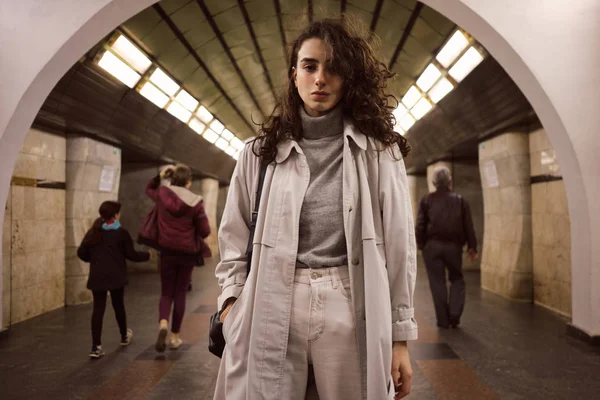 Menina casual atraente em casaco de trincheira com mochila olhando atentamente na câmera na estação de metrô — Fotografia de Stock