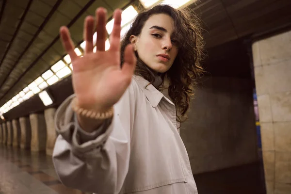 Portrait de belle fille décontractée en trench coat tirant la main à la caméra posant sensuellement à la station de métro — Photo