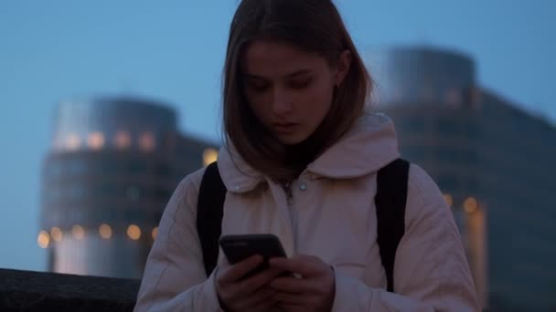 黄昏时分 美丽的女孩自信地用手机独自站在黄昏的大街上 — 图库视频影像