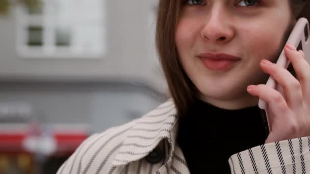 トレンチコートの魅力的な女の子の周りの追跡幸せな話上の携帯電話で街の交差点 — ストック動画