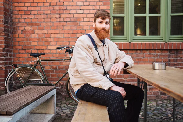 Young attractive bearded man thoughtfully looking in camera in cafe on street — 스톡 사진