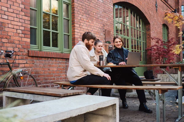 Jóvenes amigos trabajando juntos en el ordenador portátil durante el descanso de café en la cafetería al aire libre — Foto de Stock