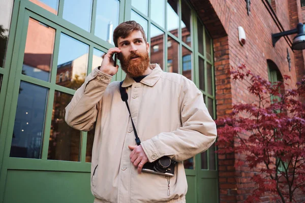Young casual bearded man intently looking away talking on cellphone outdoor — 스톡 사진