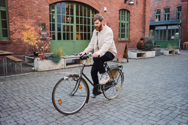 Young attractive casual man thoughtfully riding old classic bicycle through cozy city street — 스톡 사진