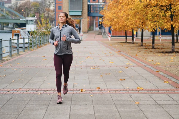 Atrakcyjna dziewczyna w sportowym stroju biegająca po pustych ulicach miasta — Zdjęcie stockowe