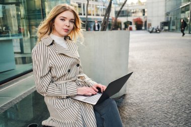 Şehir caddesinde dizüstü bilgisayarda çalışan çekici bir iş kadını.