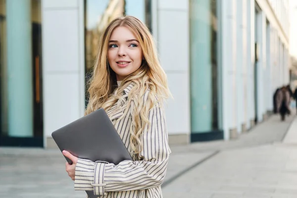 Young beautiful businesswoman with laptop happily walking through city street alone — Stock Photo, Image