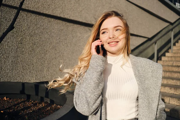 Молодая красивая блондинка разговаривает по мобильному телефону счастливо гуляя по улице в солнечный день — стоковое фото
