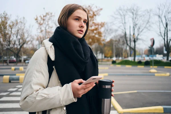 Vakre, avslappet jente med mobiltelefon som tankefullt ser bort utendørs – stockfoto
