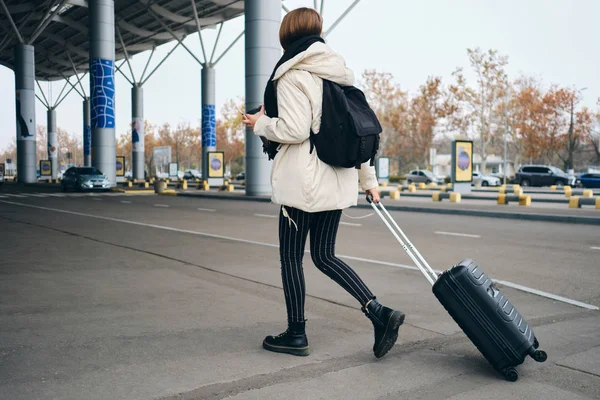 Rückansicht eines lässigen Mädchens mit Rucksack und Koffer auf dem Weg zum Flughafen — Stockfoto