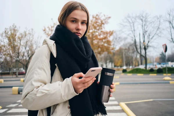 Attraktiv, tilfeldig jente med mobiltelefon som ser utendørs på kamera – stockfoto