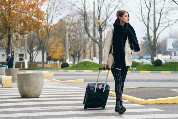 Gadis santai yang menarik hati-hati berjalan di penyeberangan dengan koper — Stok Foto