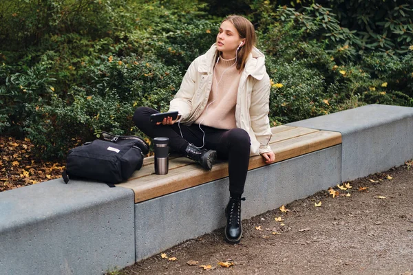 꽤 나 평범 한 소녀 가 도시 공원 벤치에서 핸드폰으로 음악을 듣고 있습니다. — 스톡 사진