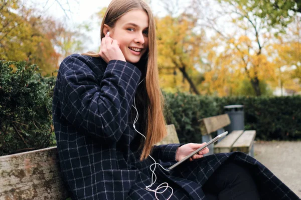 Menina muito alegre em fones de ouvido feliz descansando com tablet no banco no parque da cidade — Fotografia de Stock