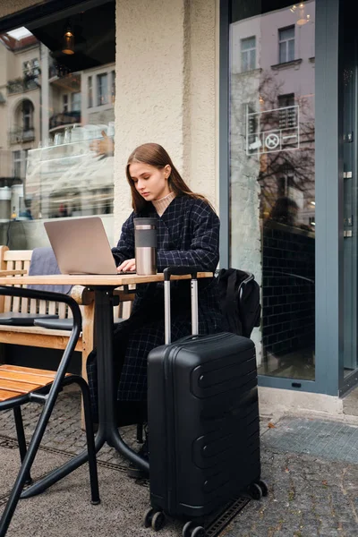 Muchacha atractiva elegante navegar por Internet sentado en la cafetería al aire libre con la maleta —  Fotos de Stock