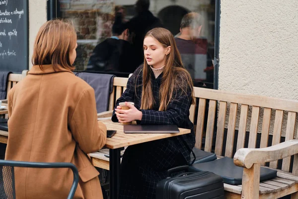 2人の魅力的なカジュアルな女の子が一緒にスーツケースと屋外カフェに座ってコーヒーを飲む — ストック写真