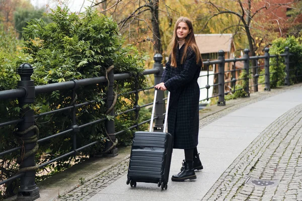 Attraktive stilvolle Mädchen im Mantel verträumt zu Fuß durch die Straße mit Koffer — Stockfoto