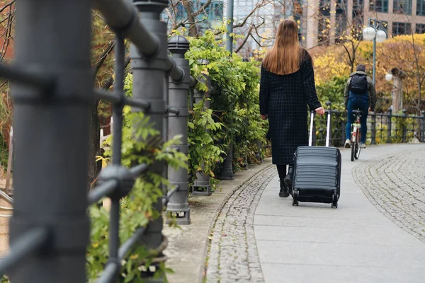 Rückansicht eines lässigen Mädchens im Mantel, das mit kleinem Koffer durch die Straße läuft — Stockfoto