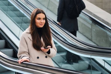 Cep telefonuyla yürüyen merdivende gülümseyen güzel esmer kız.