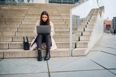 Genç ve çekici bir iş kadını laptopuyla dışarıda çalışıyor.