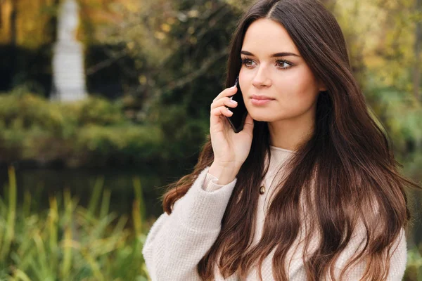 Attraktiv brunett flicka eftertänksamt tittar bort talar på mobiltelefon i vacker park — Stockfoto