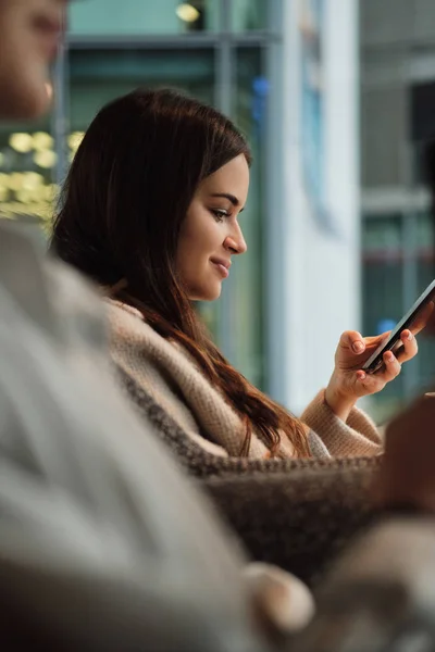 Sett fra siden av vakker, smilende jente som hviler med mobiltelefon i cefe – stockfoto