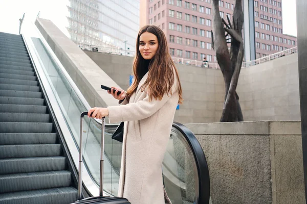 Jovem mulher de negócios elegante com mala usando escada rolante na cidade grande — Fotografia de Stock