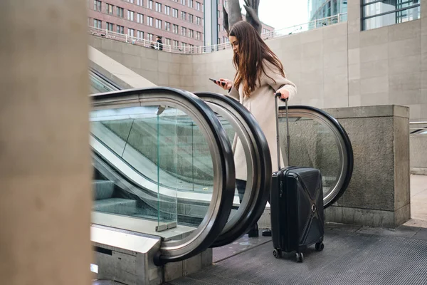 Junge attraktive Geschäftsfrau mit Koffer benutzt Rolltreppe in Großstadt — Stockfoto