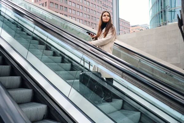 Junge schöne Geschäftsfrau mit Koffer auf Rolltreppe im Freien — Stockfoto