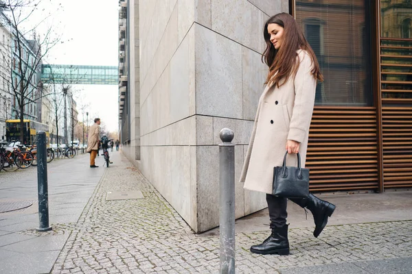 Vista lateral de la elegante chica morena en abrigo de ensueño caminando por la acogedora calle de la ciudad — Foto de Stock