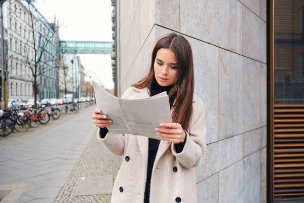 Kaunis tyylikäs brunette tyttö intensiivisesti käsittelyssä sanomalehti kaupungin kadulla — kuvapankkivalokuva