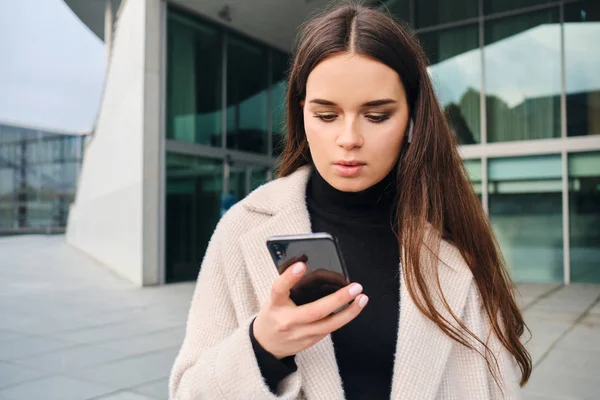 Portrett av vakker brunette-pike som har til hensikt å bruke mobiltelefon på gaten – stockfoto