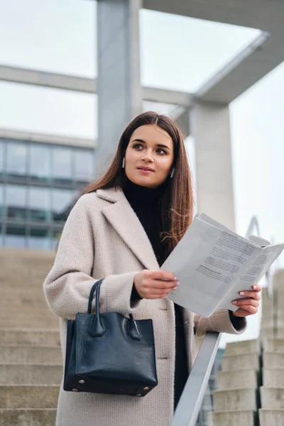 Attraktive lässige Geschäftsfrau mit Handtasche, die draußen Zeitung liest — Stockfoto