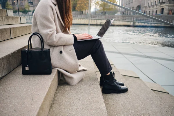 Nahaufnahme einer Gelegenheitsunternehmerin, die auf einer Treppe in der Nähe des Stadtflusses am Laptop arbeitet — Stockfoto