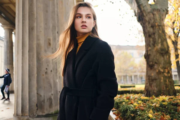 Hinreißend stylisches Mädchen im Mantel, das im herbstlichen Stadtpark aufmerksam wegschaut — Stockfoto