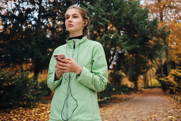 가을 파크에서 달리는 동안아름다운스 포티걸 이 휴대 전화로 음악을 듣고 있습니다. — 스톡 사진