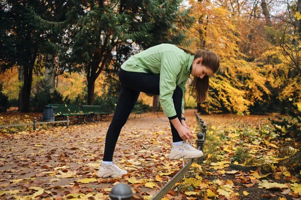 Piękna sportowa dziewczyna wiąże sznurowadła na tenisówkach przed bieganiem w przytulnym jesiennym parku — Zdjęcie stockowe