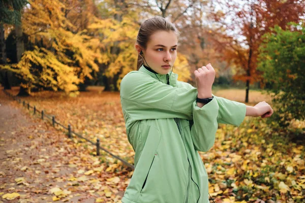Aantrekkelijk sportief meisje in oortelefoons intens stretching voor r — Stockfoto