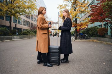 Şehrin ortasında bavulla dikilen iki çekici sıradan kızın yan görüntüsü.