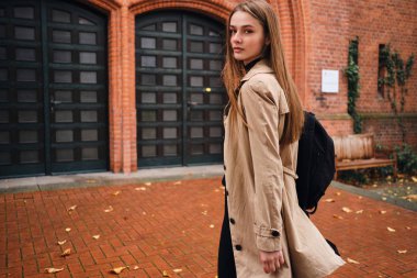 Güzel, şık bir kız sırt çantasıyla kameraya bakıyor. Sokakta tek başına dolaşıyor.