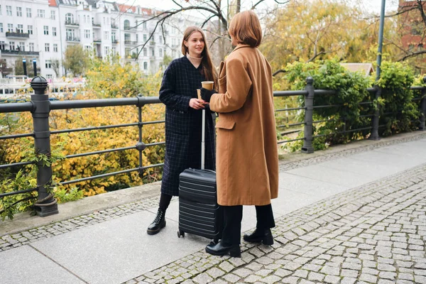 Duas meninas elegantes atraentes conversando juntos de pé com mala no parque da cidade — Fotografia de Stock