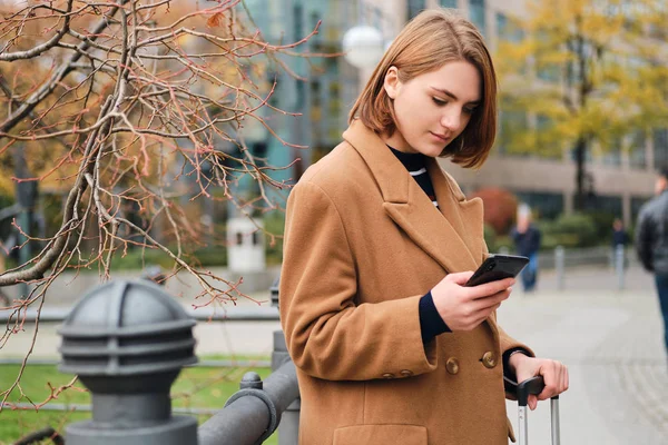 Attraktiv, stilig jente som tankefullt bruker mobiltelefon i bygata – stockfoto