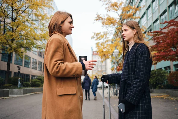 Duas meninas casuais atraentes falando de pé com mala na rua da cidade — Fotografia de Stock