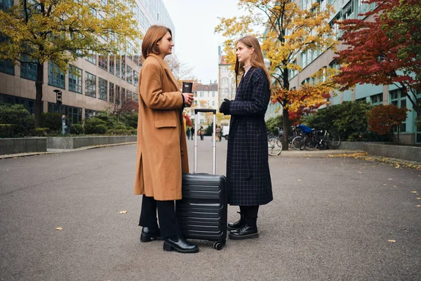 Seitenansicht zweier attraktiver, lässiger Mädchen, die mit Koffer mitten auf der Straße stehen — Stockfoto