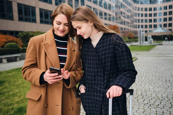Zwei attraktive Touristinnen freuen sich über Informationen über die Stadt auf dem Handy mit Koffer im Freien — Stockfoto